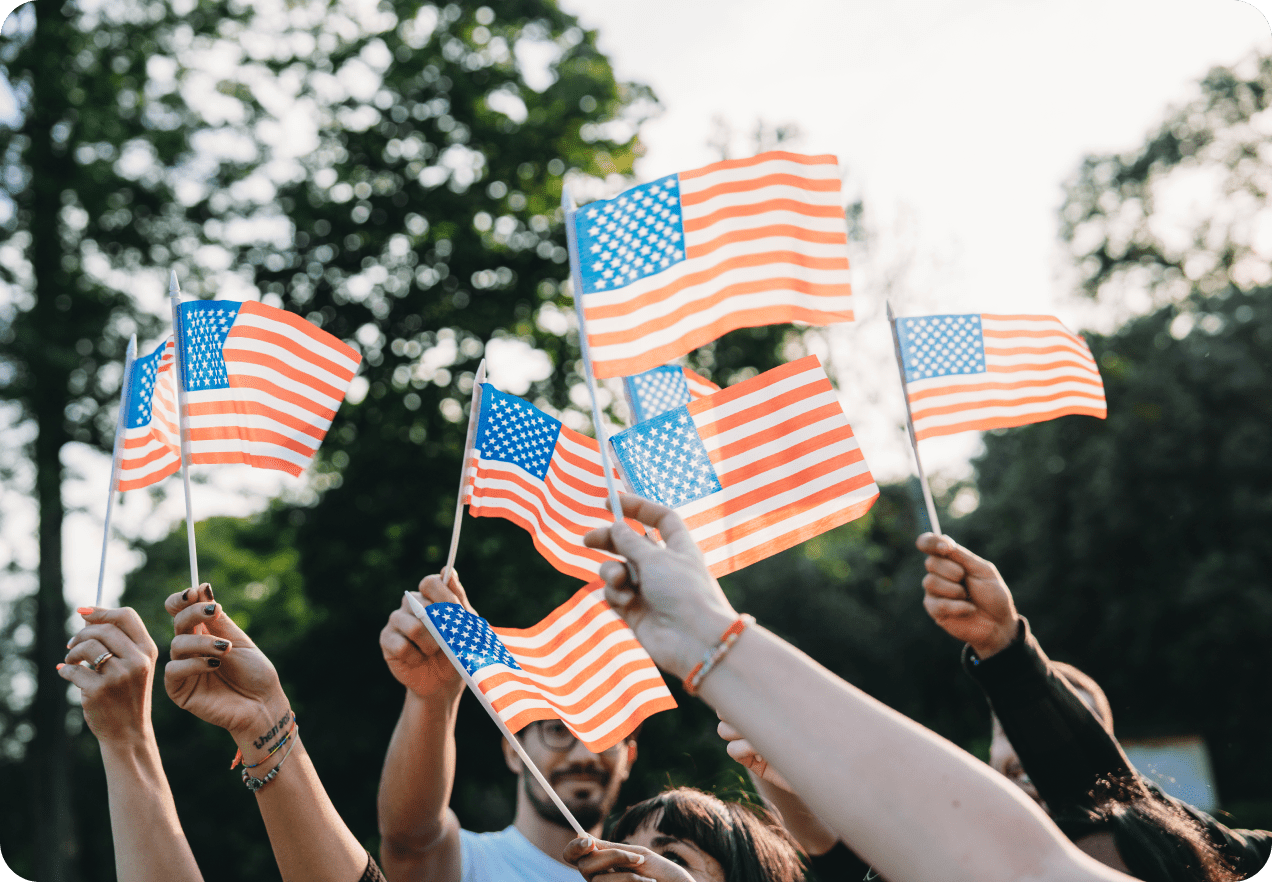 People holding small American flags, outdoors with trees in the background.