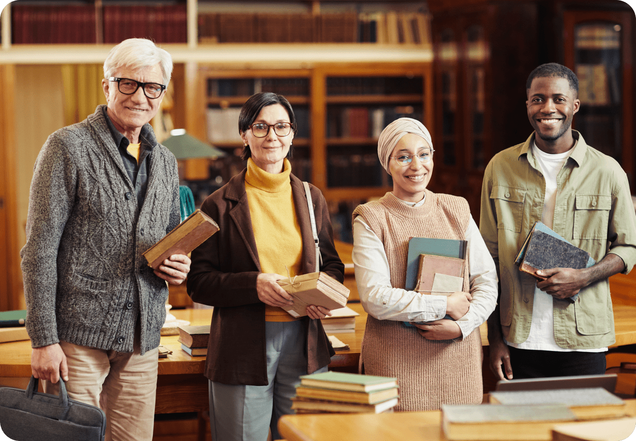 Four people standing in a library, holding books and smiling.