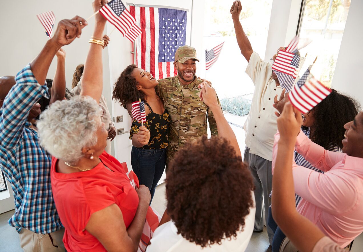 GettyImages-1137017235 A group of people standing around each other holding american flags.