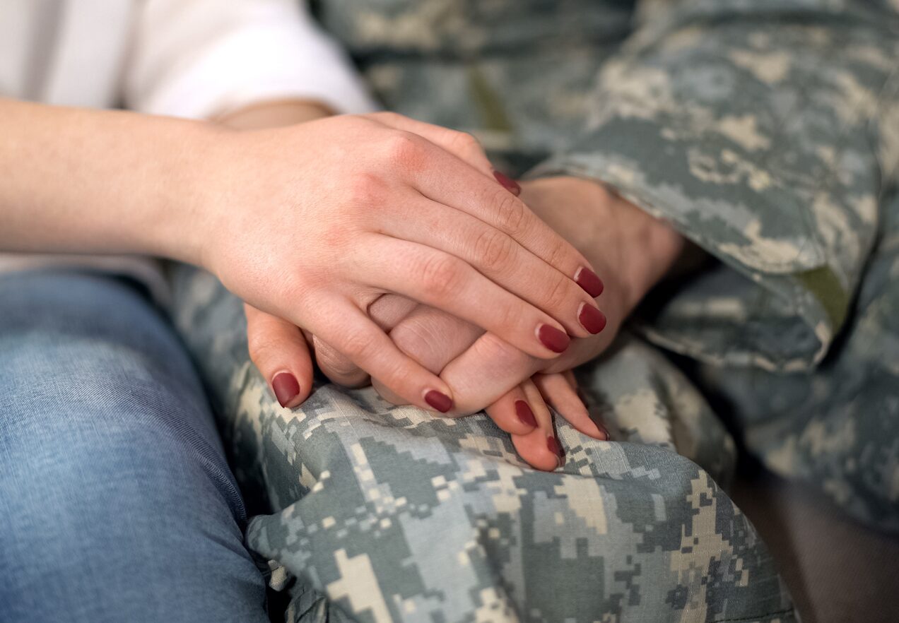 GettyImages-1168236548 A woman holding hands with another person in fatigues.