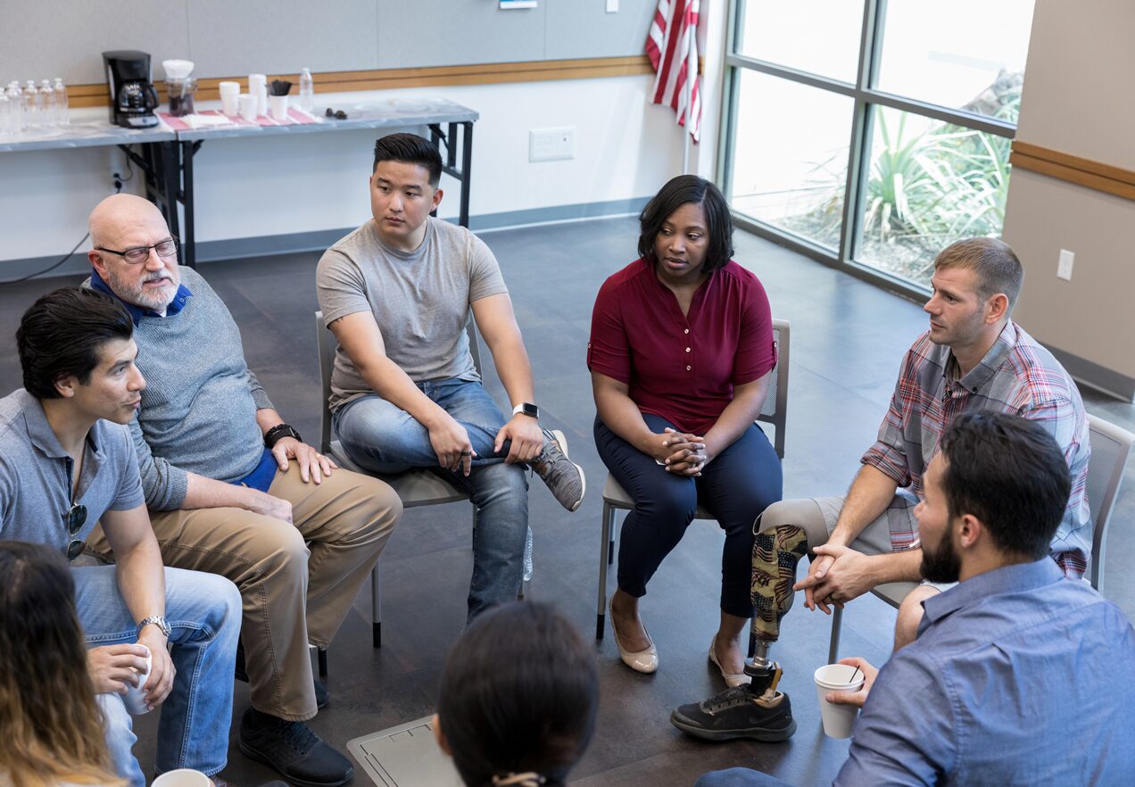 GettyImages-1174211791 A group of people sitting in chairs around each other.