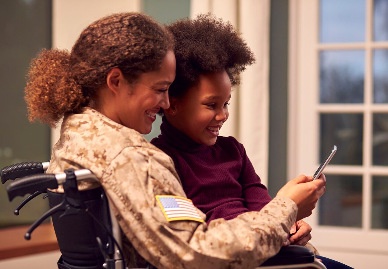 GettyImages-1366941856 A woman in a wheelchair and a girl looking at a cell phone.