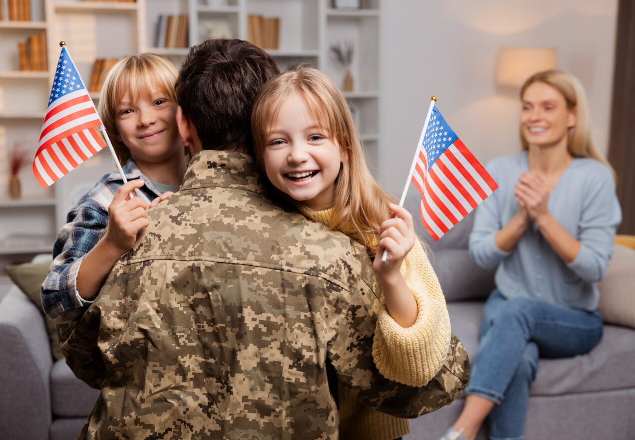 GettyImages-2064388045 A soldier is hugging his family and holding an american flag.