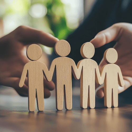 Wooden family figures protected by hands.