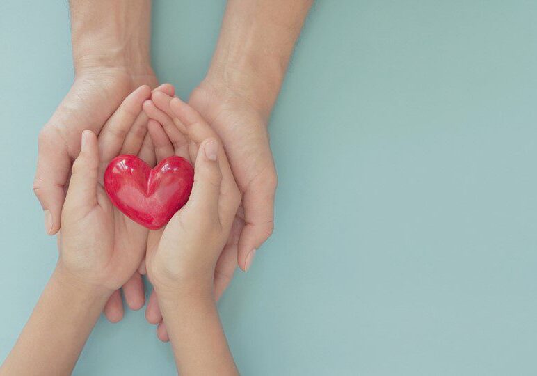 Adult and child hands holding red heart.